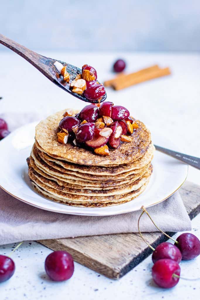 Oatmeal Pancakes topped with cherry almonds spooned on top with wooden spoon