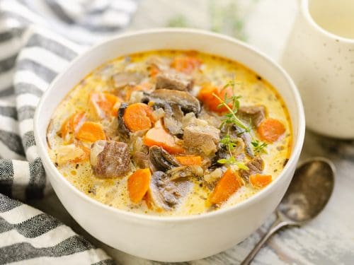 Creamy Mushroom Beef Soup in white bowl with stripe napkin