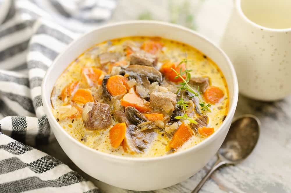 Creamy Mushroom Beef Soup in white bowl with stripe napkin