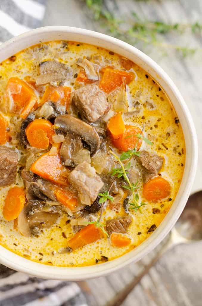 Creamy Mushroom Beef Soup in white bowl on table with thyme