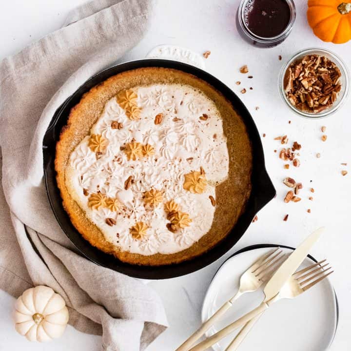 Pumpkin Spicy Dutch Baby on white table with pumpkins, silverware, pecans and maple syrup