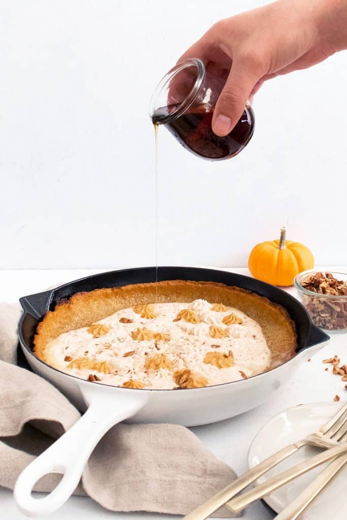 Pumpkin Spicy Dutch Baby in cast iron skillet drizzled with cup of maple syrup