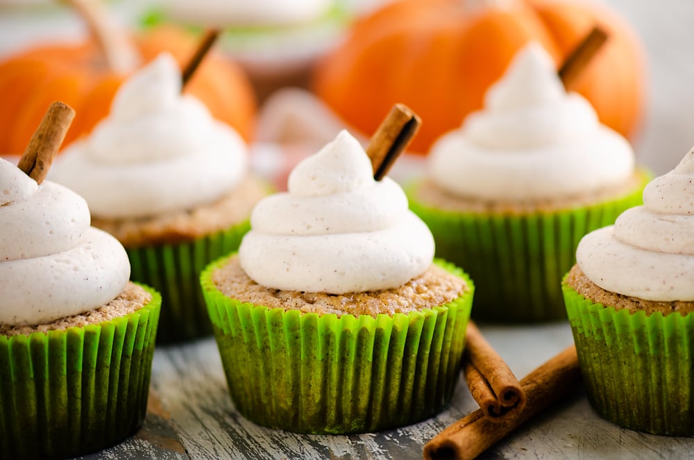 fall spiced cupcakes with buttercream swirls on table with cinnamon and pumpkins