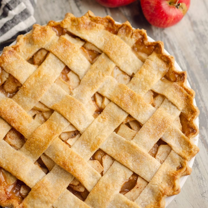 Old Fashioned Apple Pie with lattice crust on table with apples