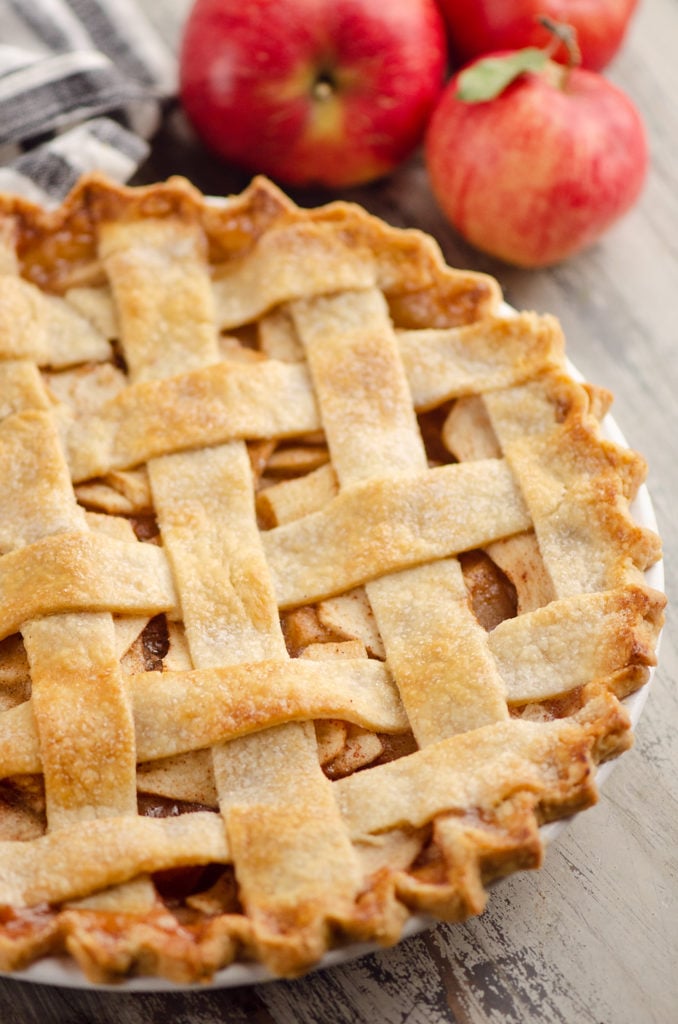 Old Fashioned Apple Pie with lattice crust on table with apples