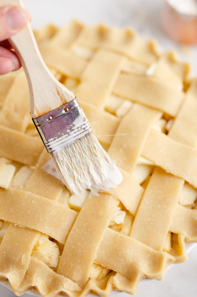 pastry brush putting cream on lattice crust of apple pie