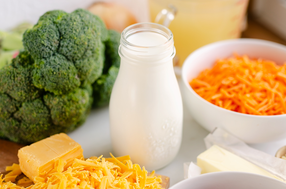 marble table with glass jar of milk, broccoli, cheese, carrots and butter