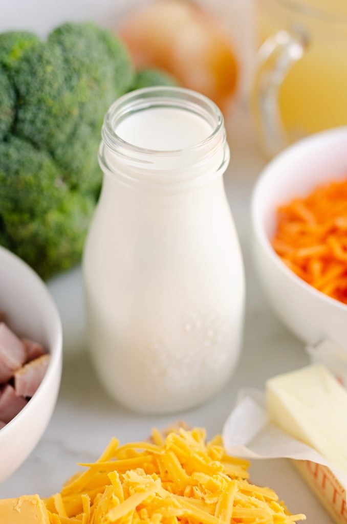 marble table with glass jar of milk, broccoli, cheese, carrots and butter