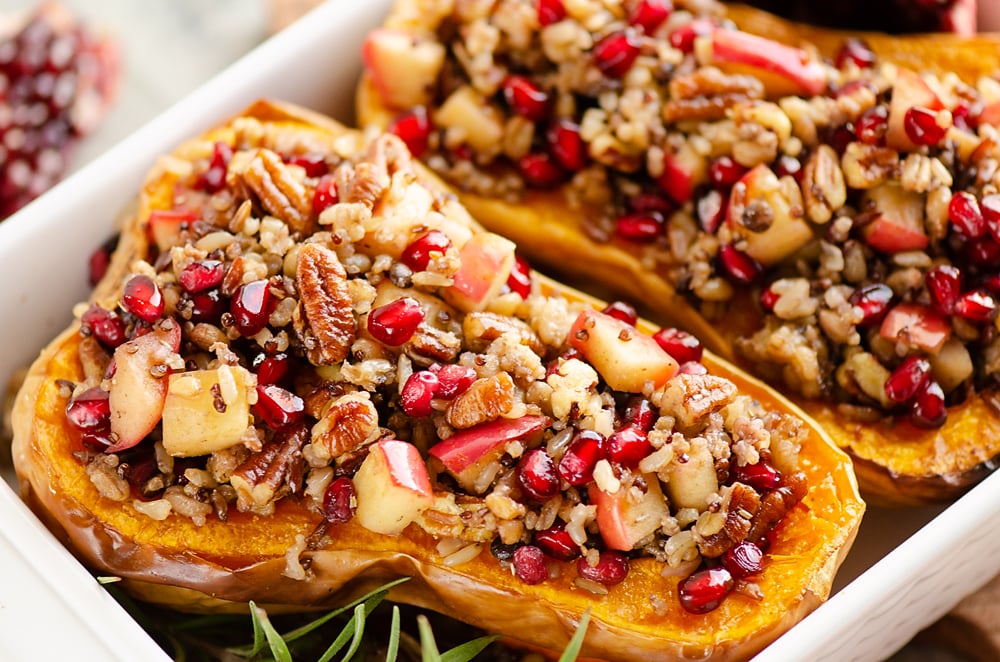 Stuffed Butternut Squash with Apples, Pomegranates & Grains in white baking pan with rosemary
