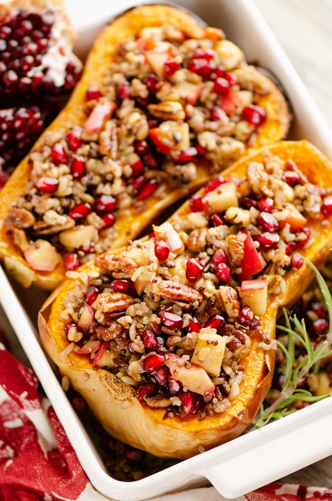 Stuffed Butternut Squash with Apples, Pomegranates & Grains in baking dish with fresh rosemary