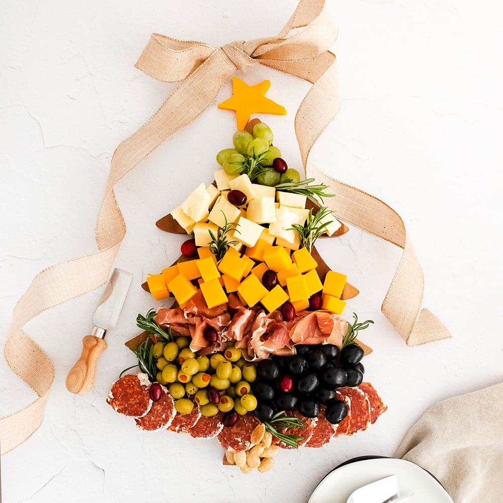 christmas tree cutting board topped with meat and cheese and a burlap bow