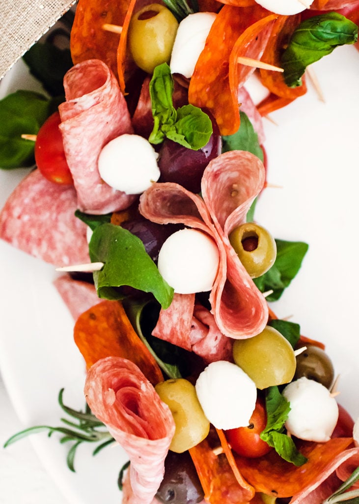 skewers of meat, cheese, olives, tomatoes and basil on white plate