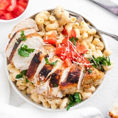 cajun chicken breasts sliced over alfredo pasta in white bowl