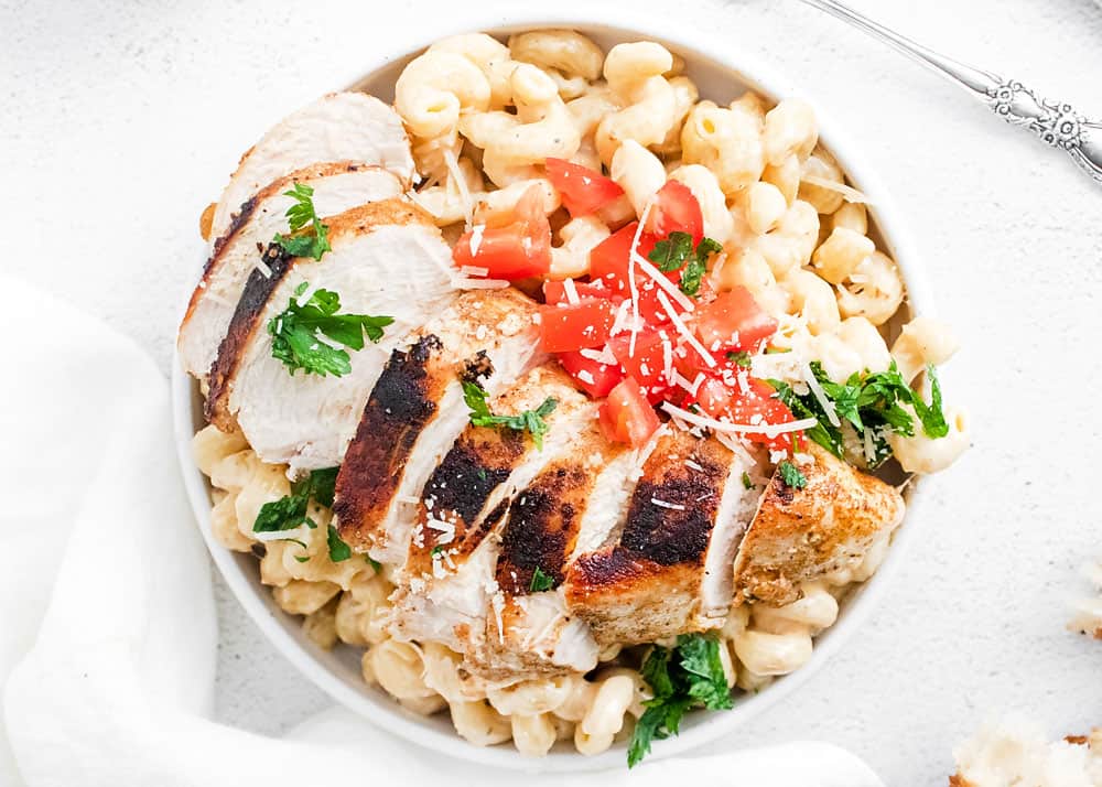 cajun chicken breasts sliced over alfredo pasta in white bowl topped with tomatoes