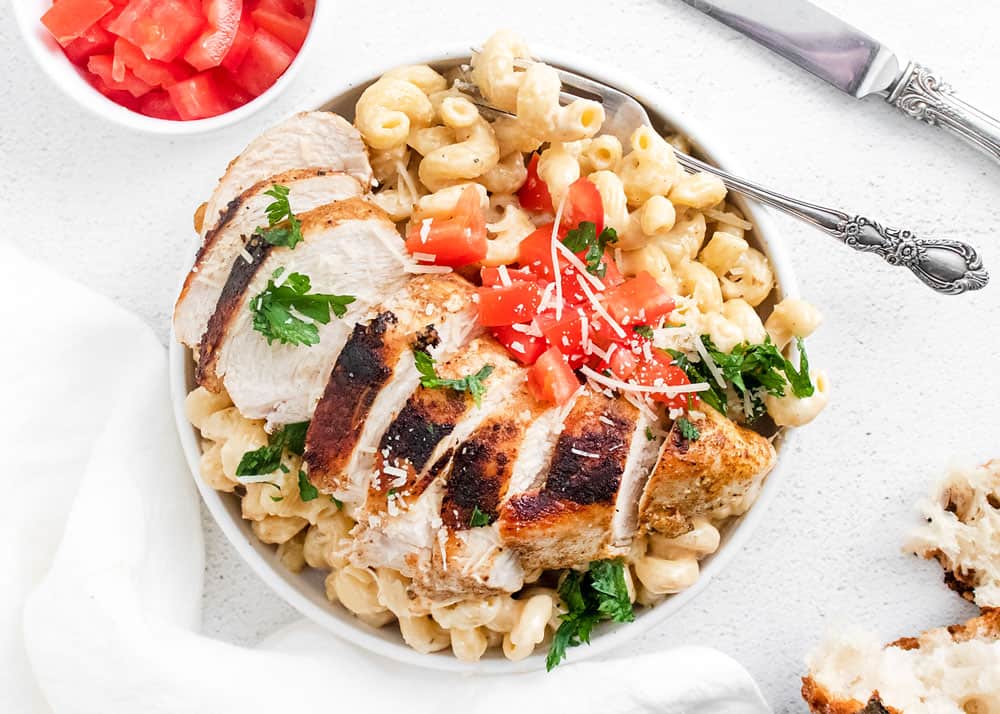 cajun chicken breasts sliced over alfredo pasta in white bowl