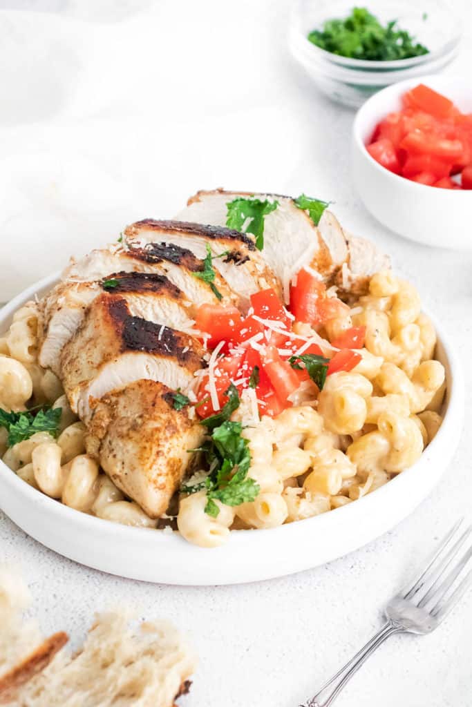 cajun chicken breasts sliced over alfredo pasta in white bowl