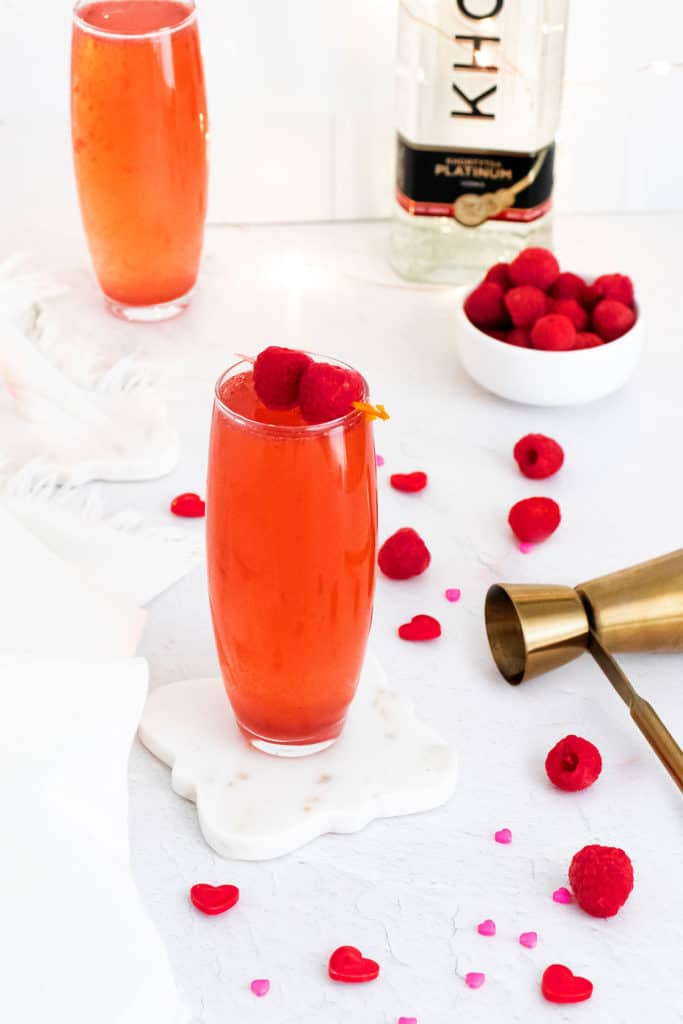 Raspberry Rosé Spritzer on table with shot pourer and bowl of raspberries