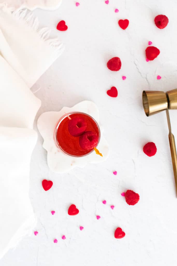 Raspberry Rosé Spritzer on table with shot pourer and bowl of raspberries