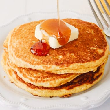 syrup being poured on cornmeal pancakes