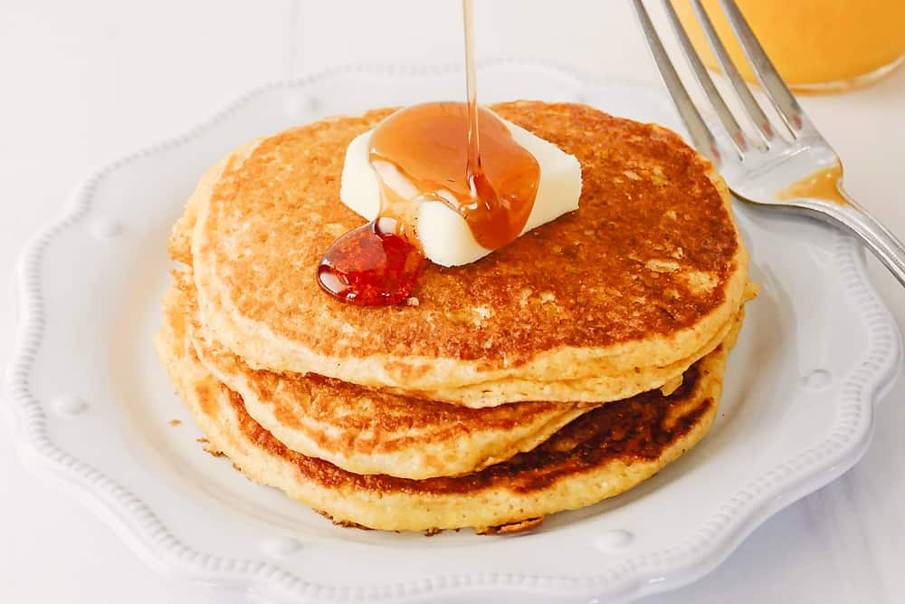 syrup being poured on cornmeal pancakes