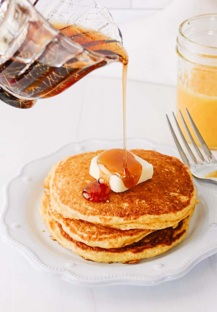 syrup being poured on cornmeal pancakes with butter