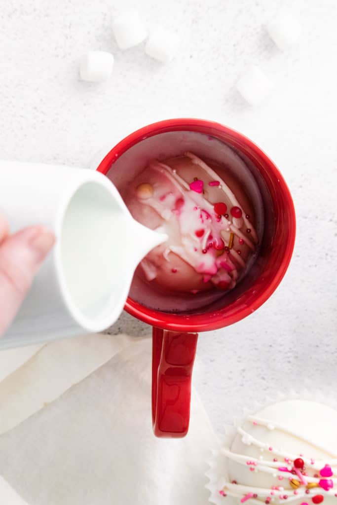 pouring milk over hot cocoa bomb in red mug