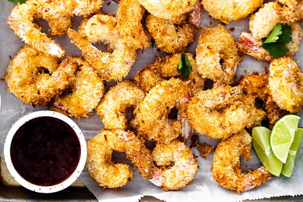 coconut shrimp on sheet pan with parchment with limes and sweet chili dipping sauce