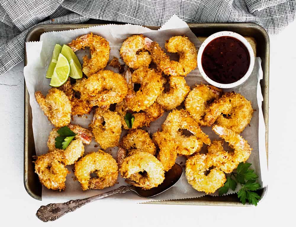 coconut shrimp on sheet pan with parchment with limes and sweet chili dipping sauce