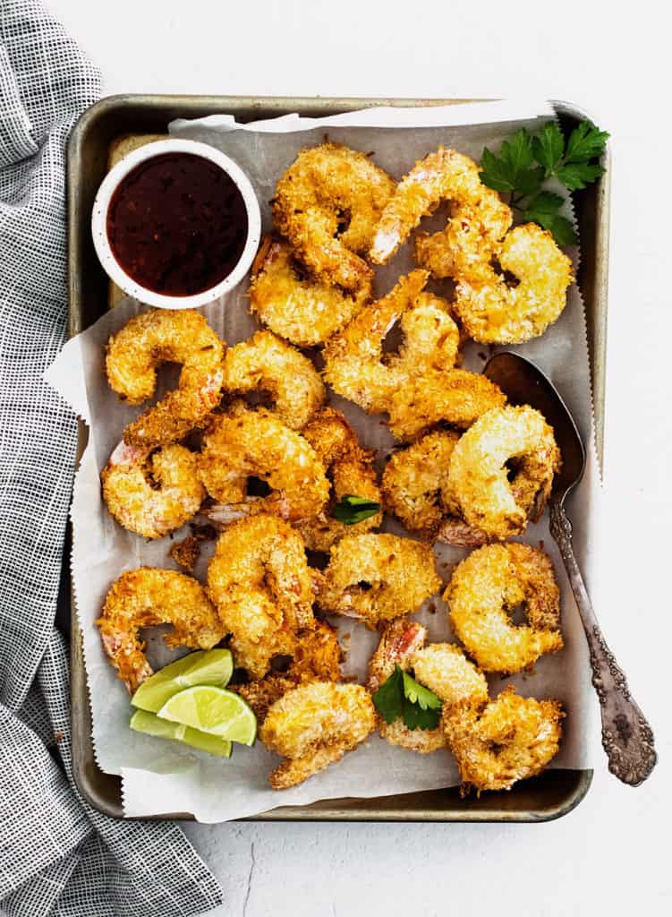 coconut shrimp on sheet pan with parchment with limes and sweet chili dipping sauce