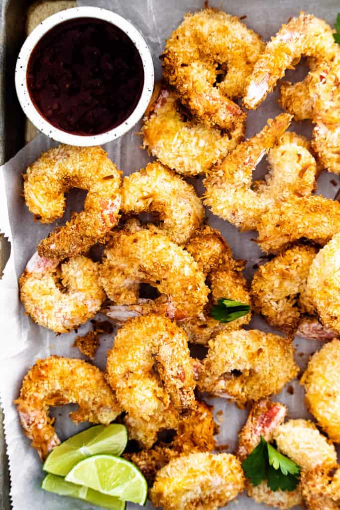 coconut shrimp on sheet pan with parchment with limes and sweet chili dipping sauce