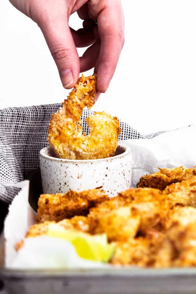 coconut shrimp being dipped in bowl of sweet chili sauce