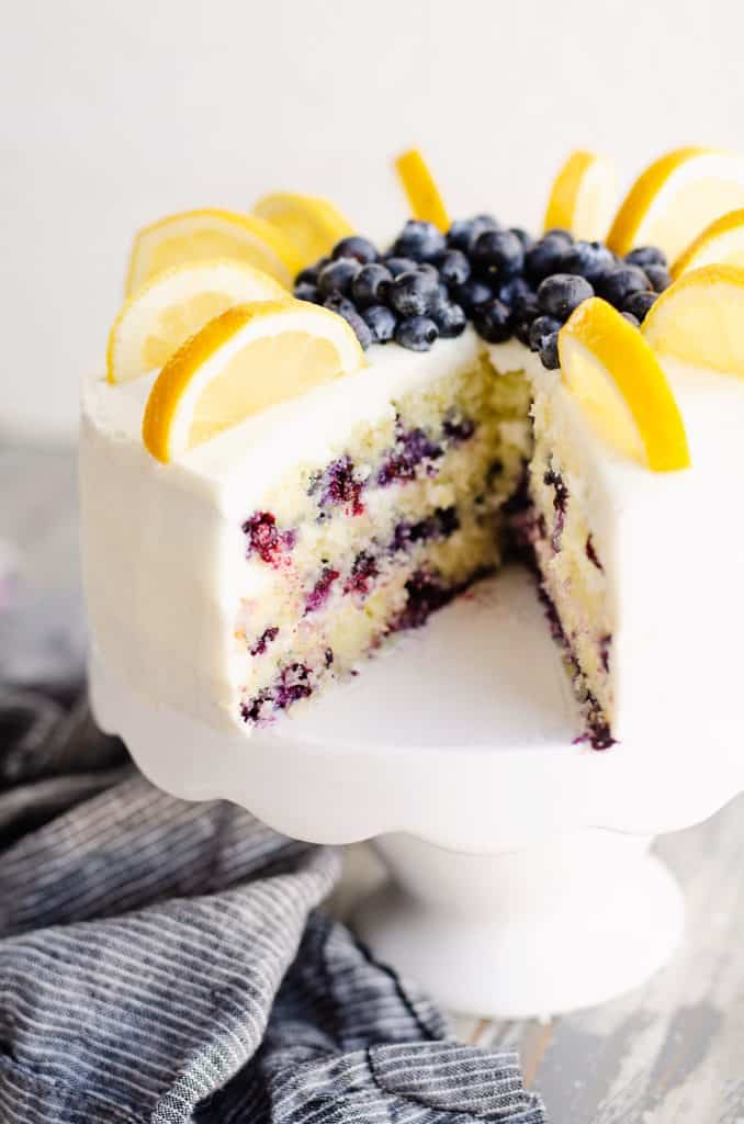 blueberry lemon cake on stand with piece of cake cut out