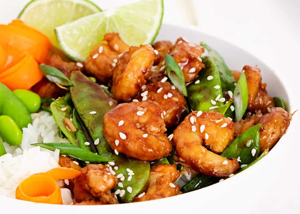 sesame shrimp and vegetables in white bowl with lime wedges