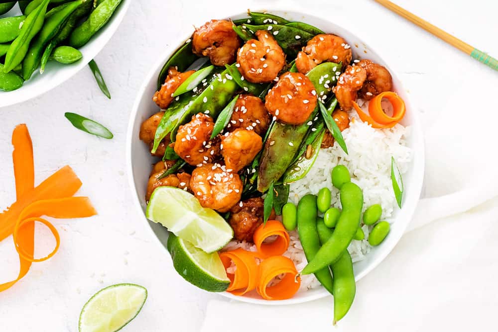 edamame, carrots, rice, lime, peas and shrimp in bowl with chopsticks