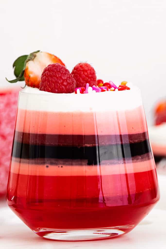 red layered jello in glass cup with Cool Whip and berries