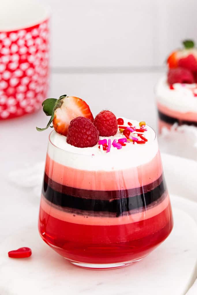 red layered jello in glass cup with Cool Whip and berries