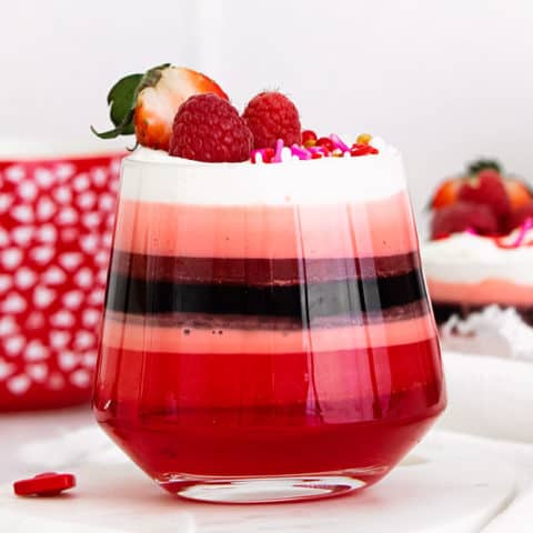 red layered jello in glass cup with Cool Whip and berries