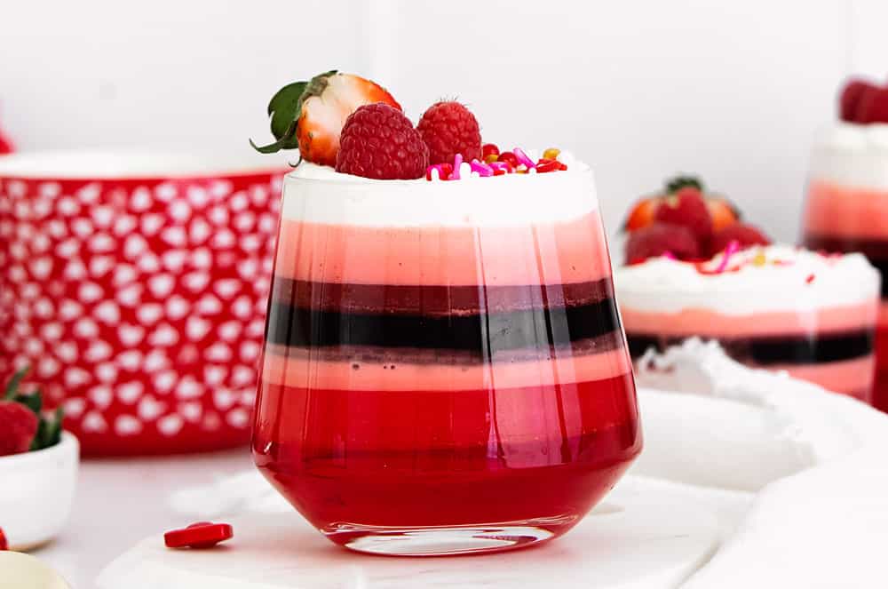 red layered jello in glass cup with Cool Whip and berries