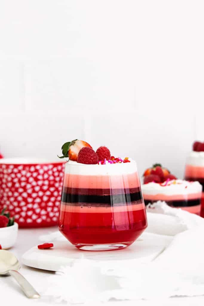 red layered jello in glass cup with Cool Whip and berries
