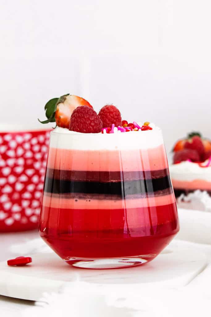 red layered jello in glass cup with Cool Whip and berries