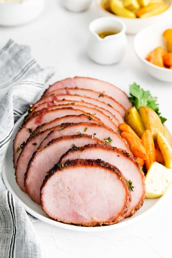 sliced ham on white platter with vegetables