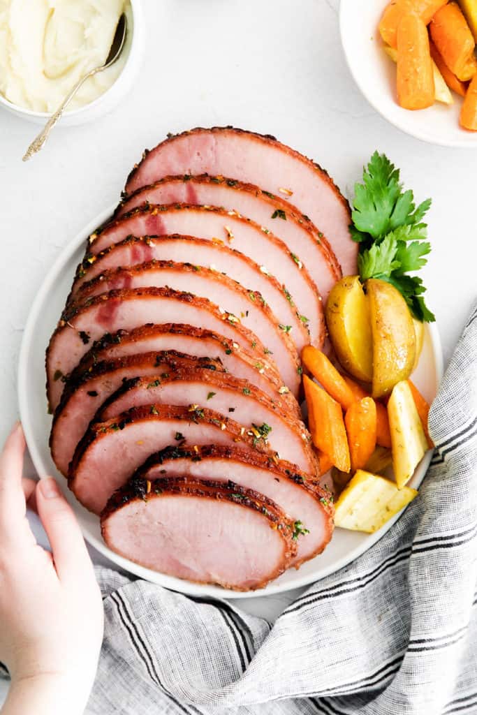 hand holding white platter with sliced herb ham