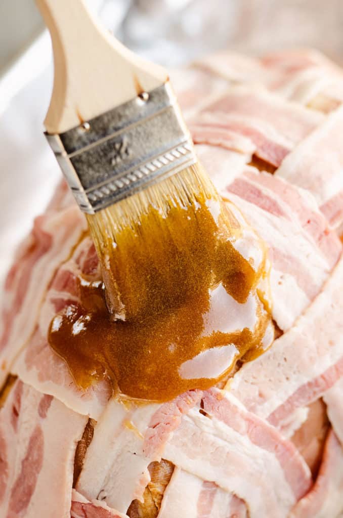 maple dijon glaze being brushed on bacon wrapped ham