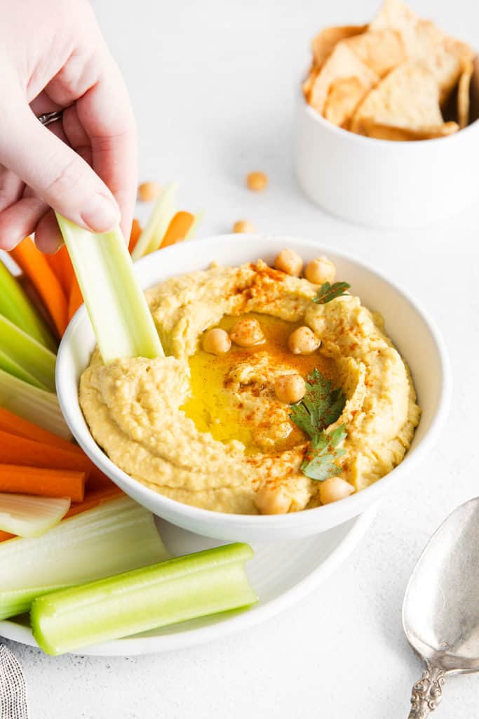 celery dipped in bowl of class hummus