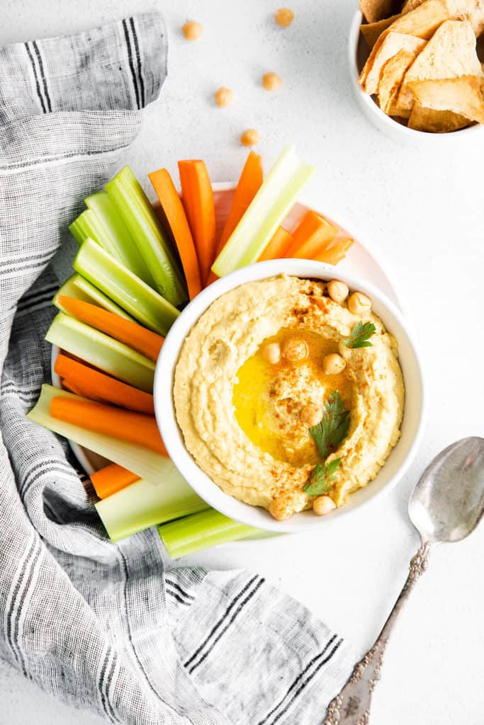 plate with bowl of classic hummus, vegetables on table with bowl of bread and spoon