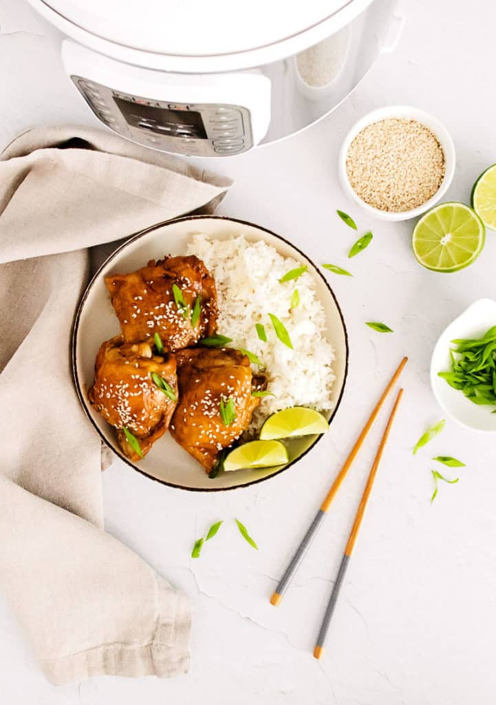 honey soy glazed chicken thigh in bowl with lime wedges, rice and sesame seeds