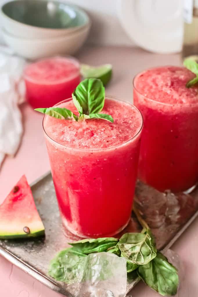 watermelon wine slushies on table with basil leaves and watermelon wedges