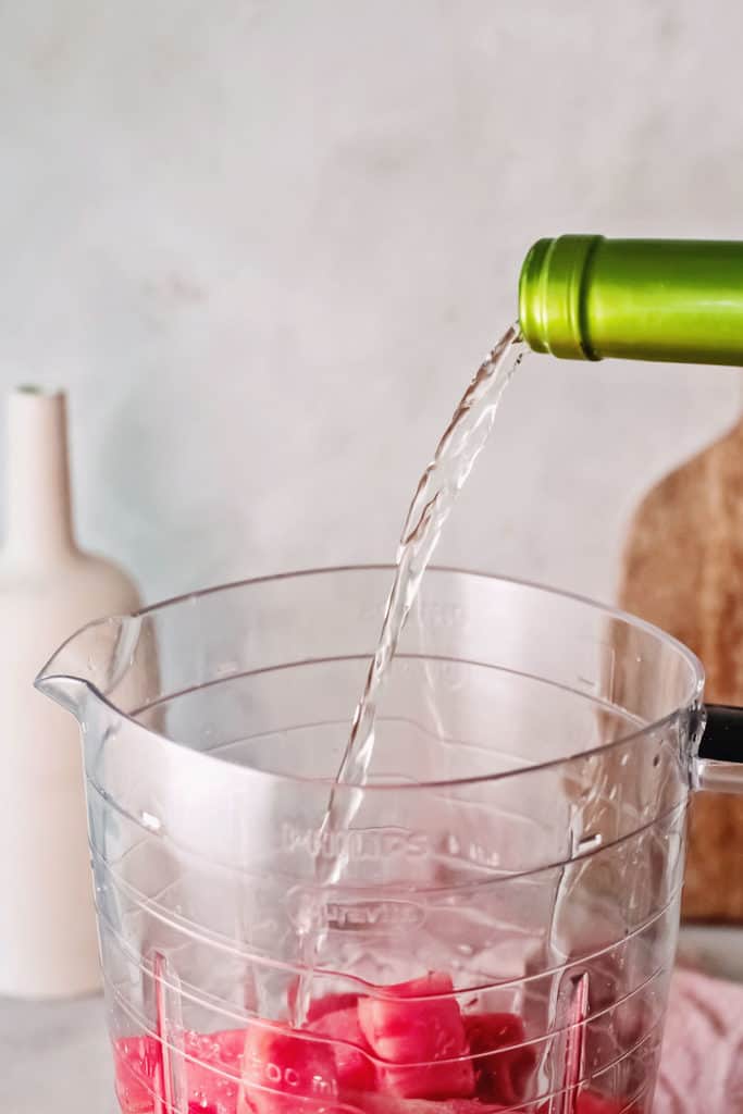 white wine being poured into blender with cubed watermelon