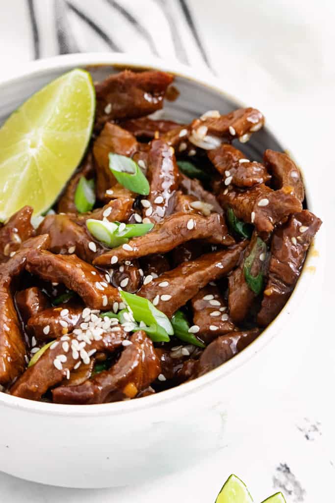 sesame beef with a lime wedge in white bowl