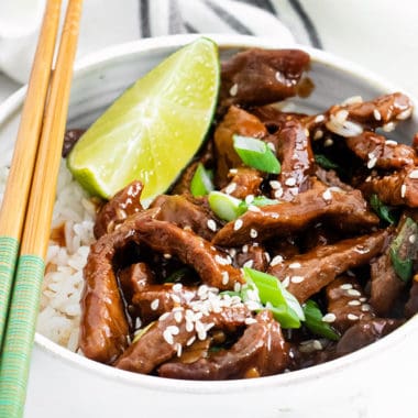 bowl of sesame beef with white rice topped with chopsticks